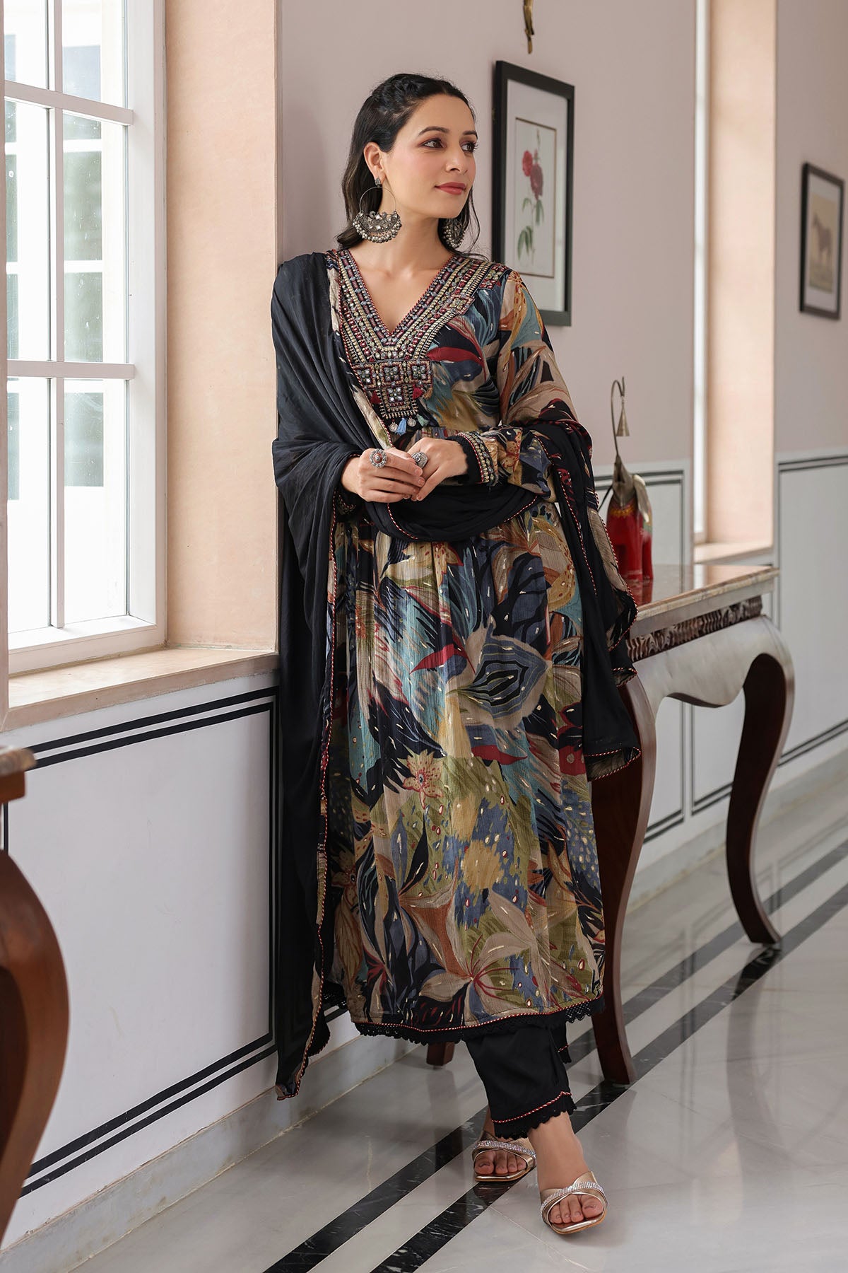 Woman in a patterned dress standing in a room with white walls and a window.