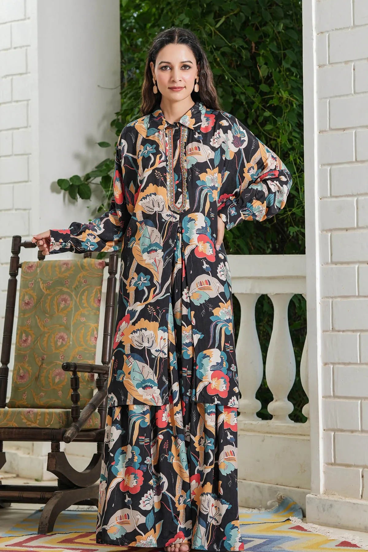Woman in a floral dress standing on a porch with a chair and plants in the background.