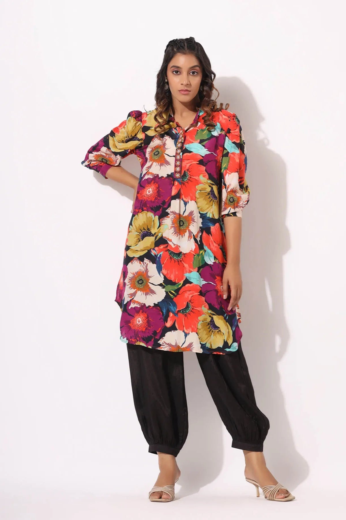 Woman wearing a colorful floral dress with black pants on a white background