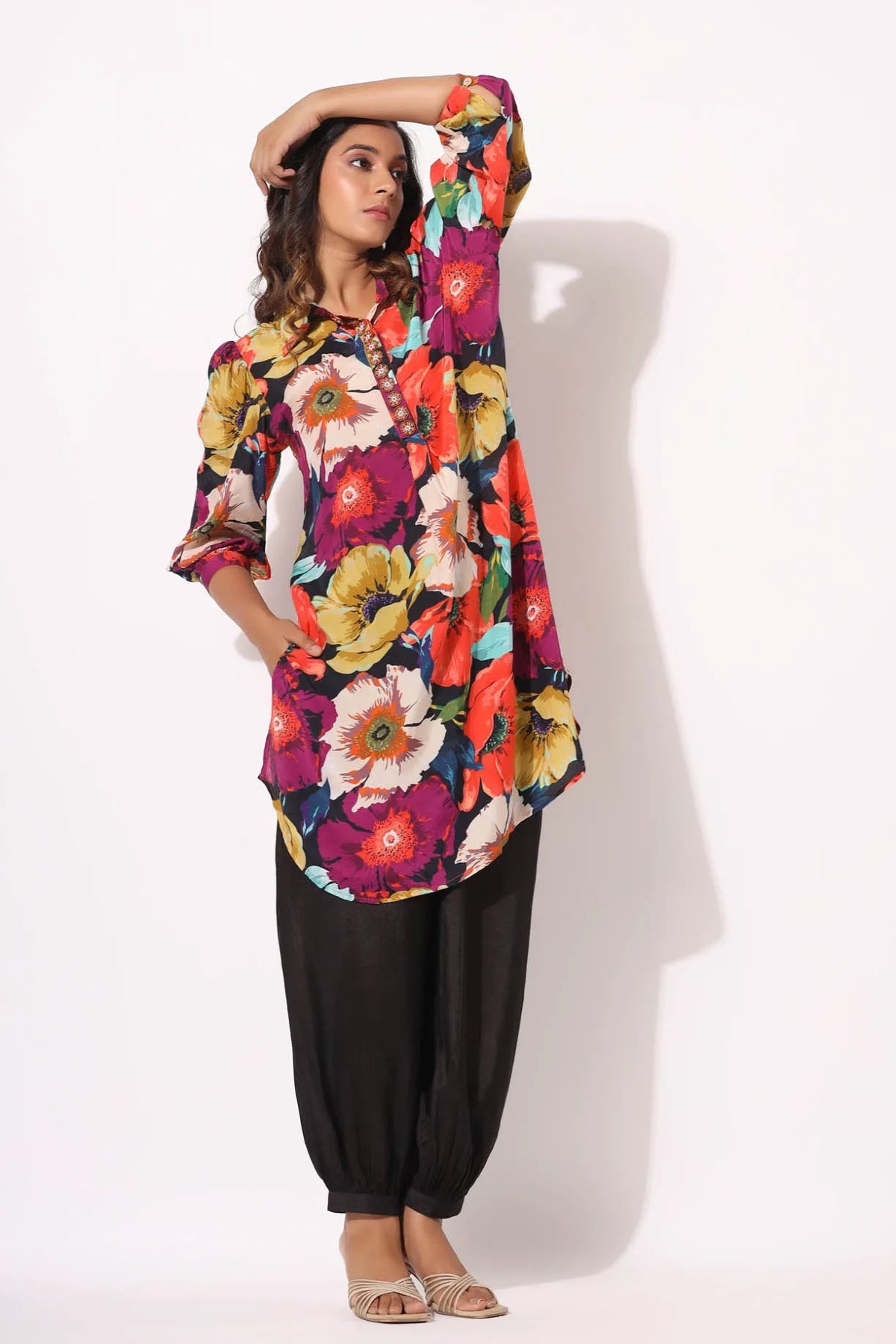 Woman wearing a colorful floral top and black pants on a white background