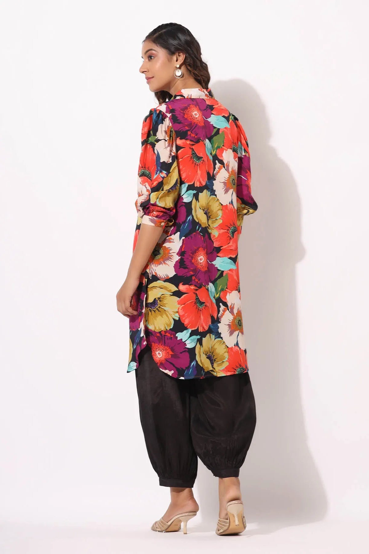 Woman wearing a colorful floral dress with black pants on a white background
