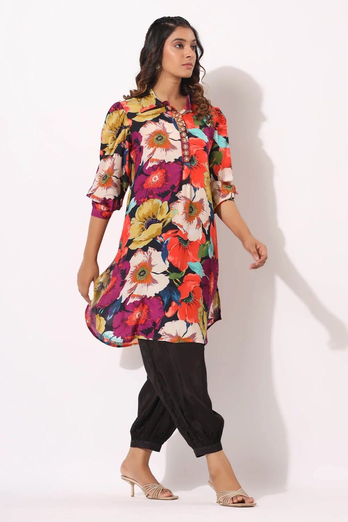 Woman wearing a colorful floral dress with black pants on a white background