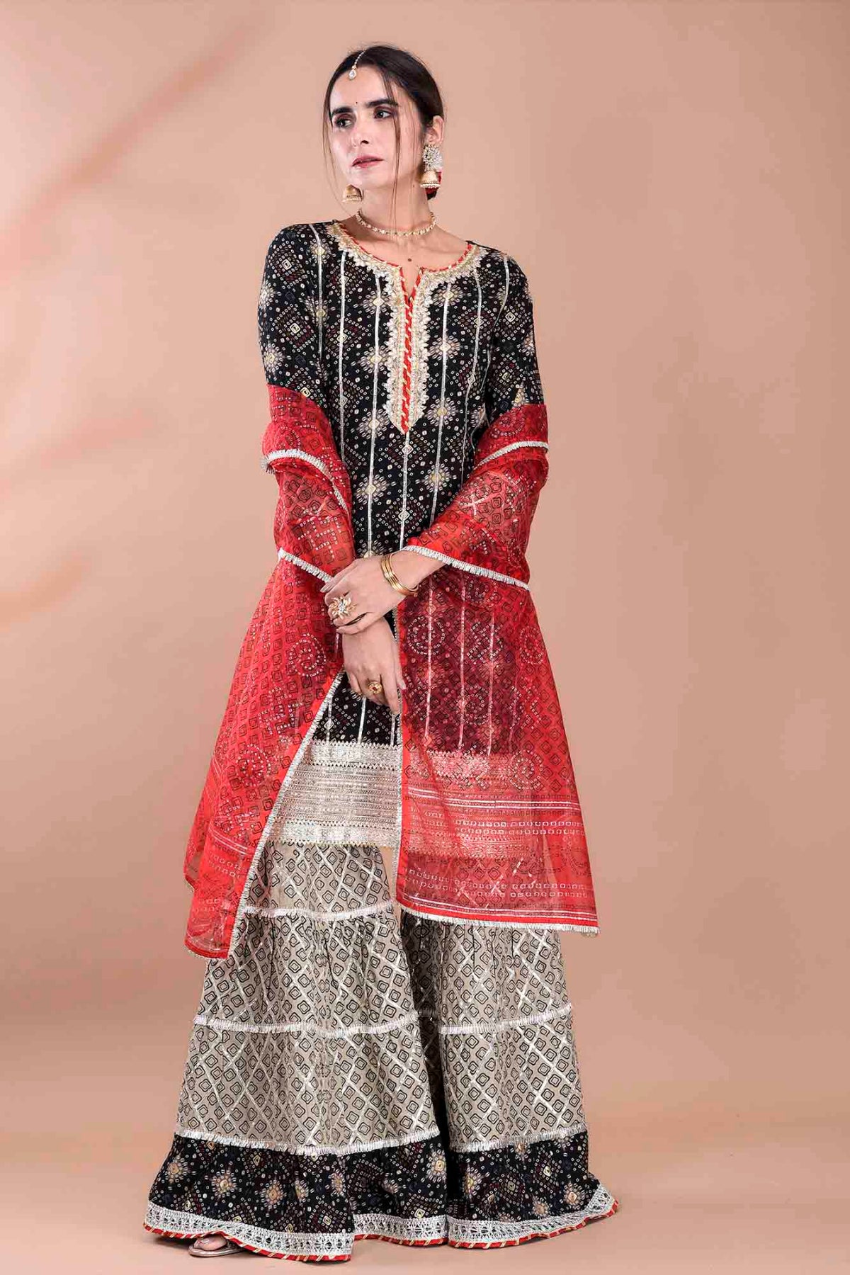 Woman wearing a traditional outfit with a red and black patterned top and white and black patterned pants on a beige background.