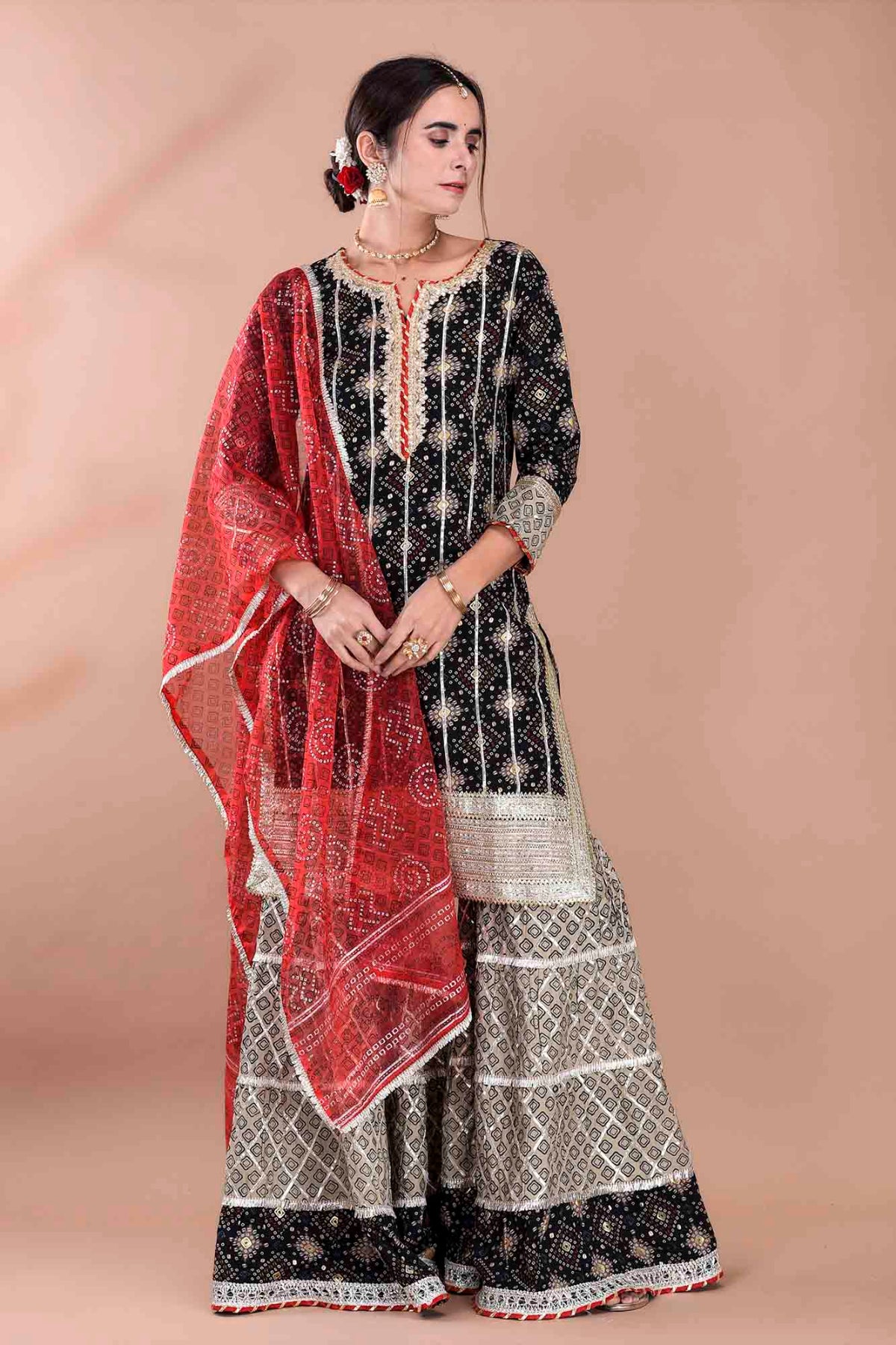 Woman wearing a traditional outfit with a black and white patterned dress and red dupatta on a beige background
