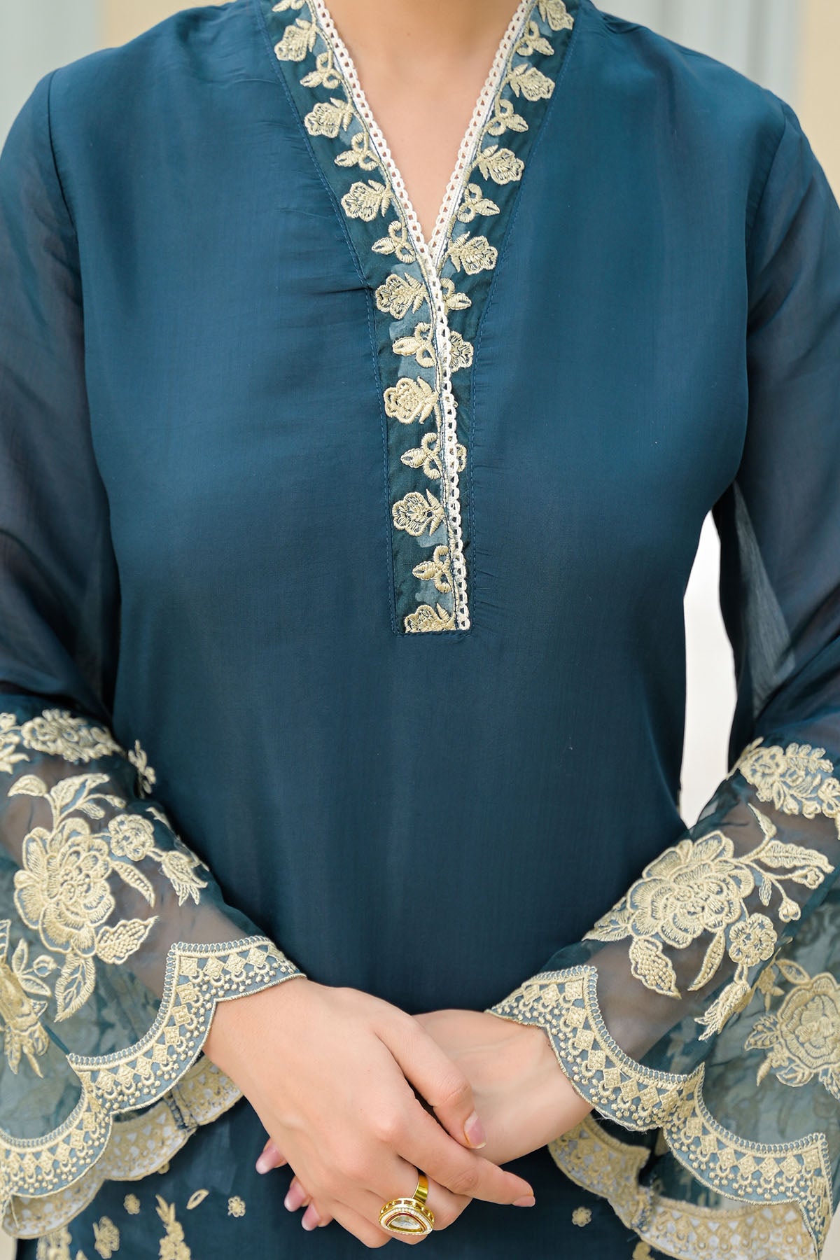 Teal blouse with floral embroidery on neckline and sleeves against a neutral background