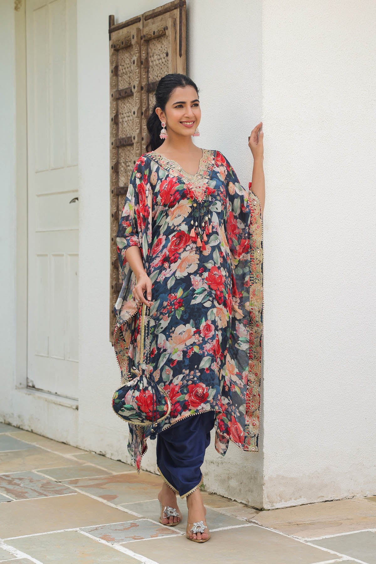 Woman wearing a floral dress standing in front of a white wall with a wooden door.