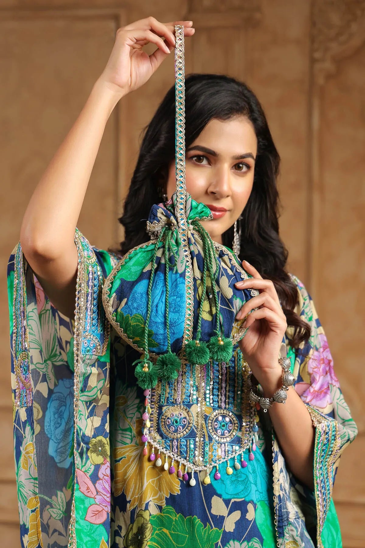 Woman holding a decorative bag with intricate designs against a beige wall.