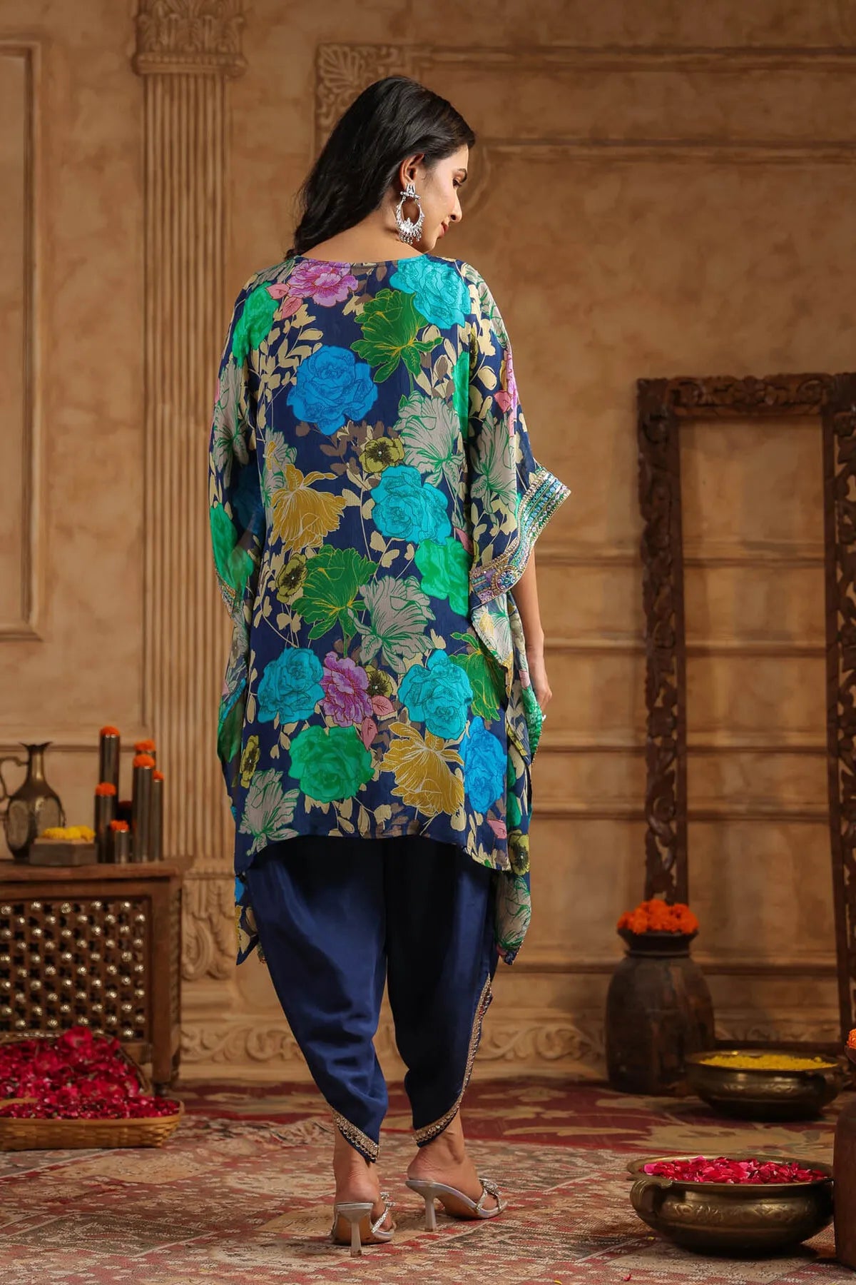 Woman wearing a colorful floral top and blue pants in an ornate room.