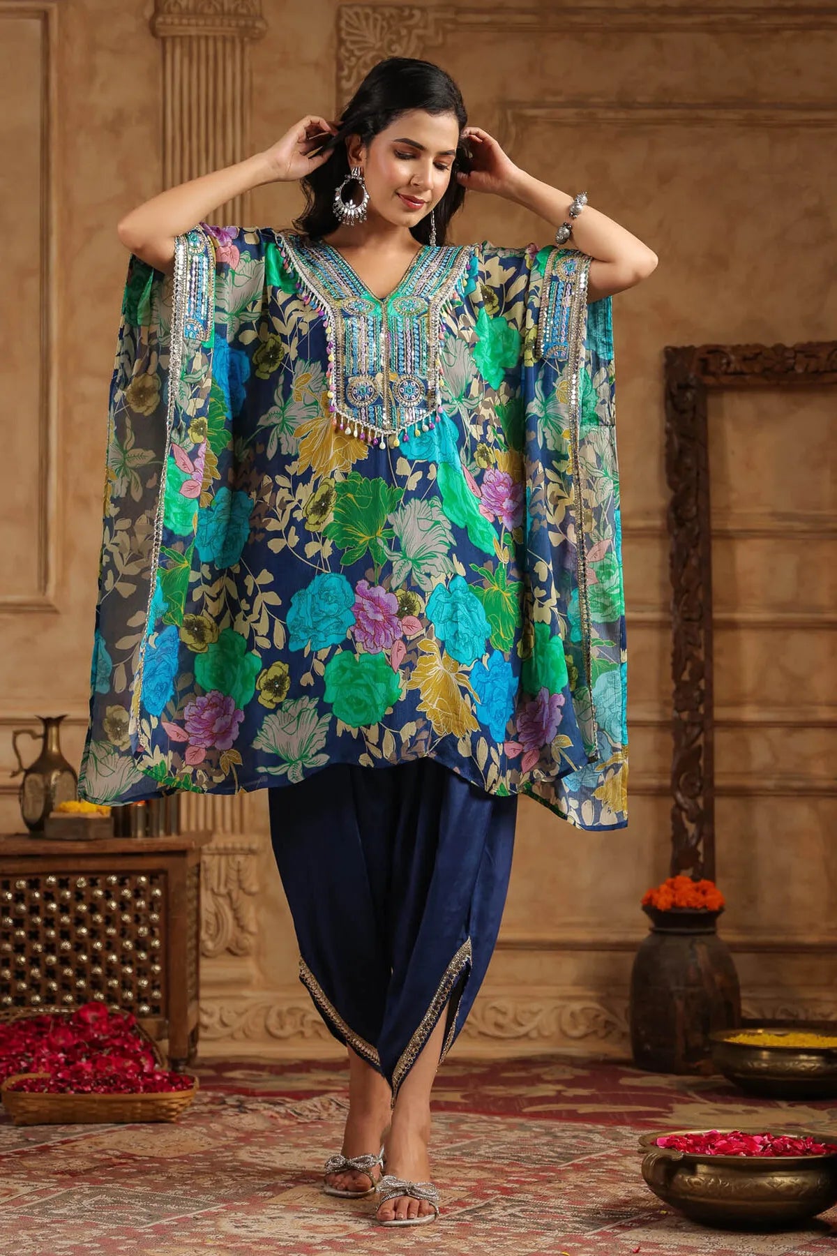 Woman wearing a colorful floral dress with a blue dupatta in an ornate room.
