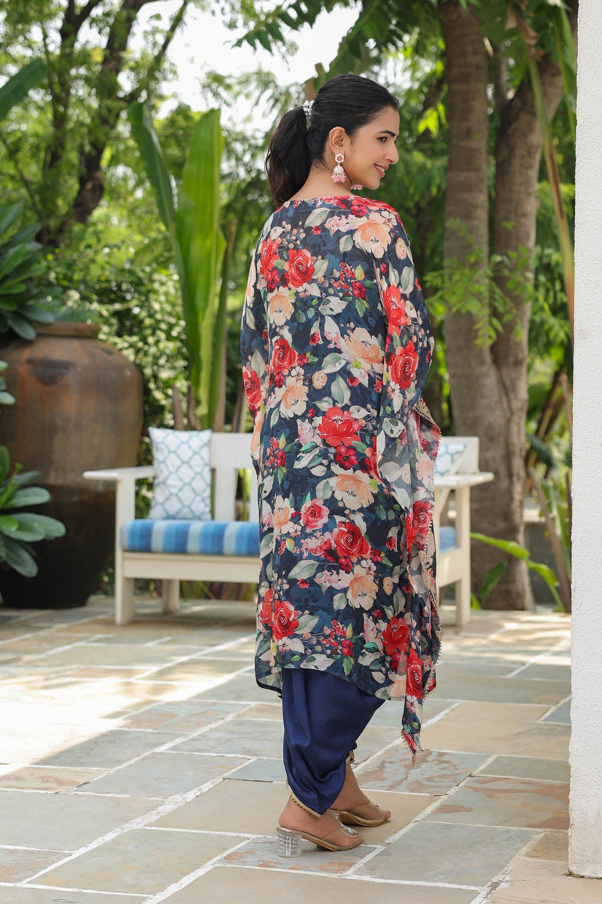 Woman wearing a floral dress in an outdoor setting with trees and a bench.
