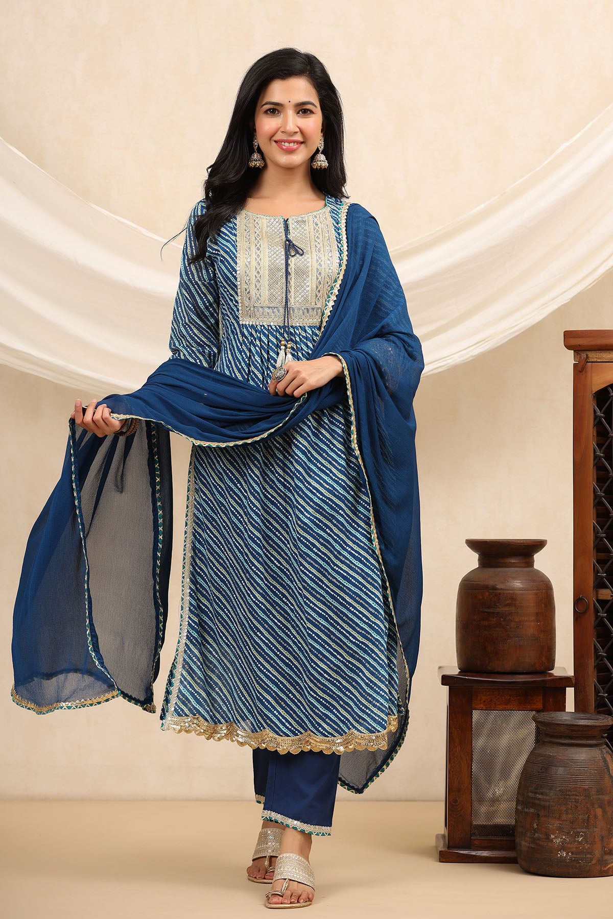 Woman wearing a blue and white traditional outfit with a matching dupatta against a beige background.
