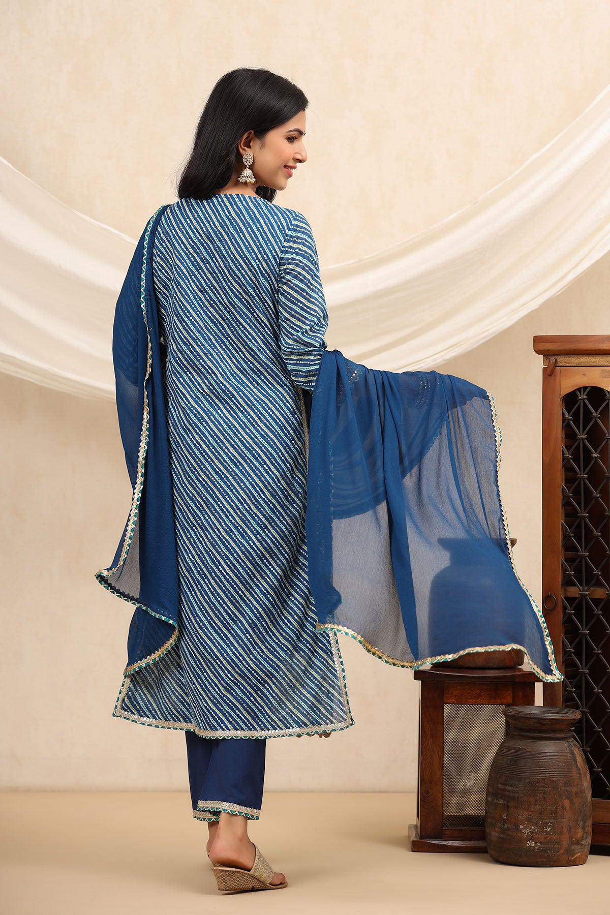 Woman wearing a blue traditional outfit with a sheer dupatta against a beige background
