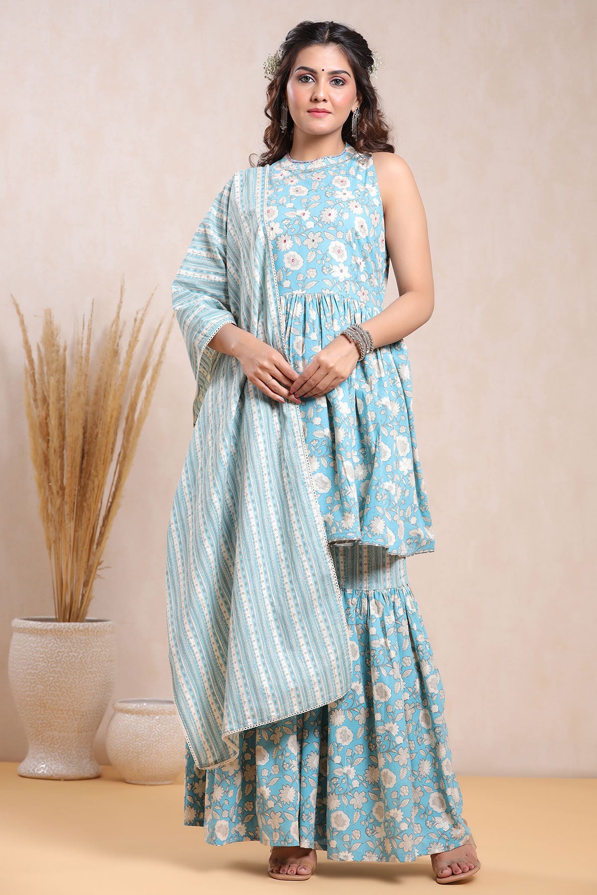 Woman wearing a light blue floral dress with a matching dupatta against a beige background