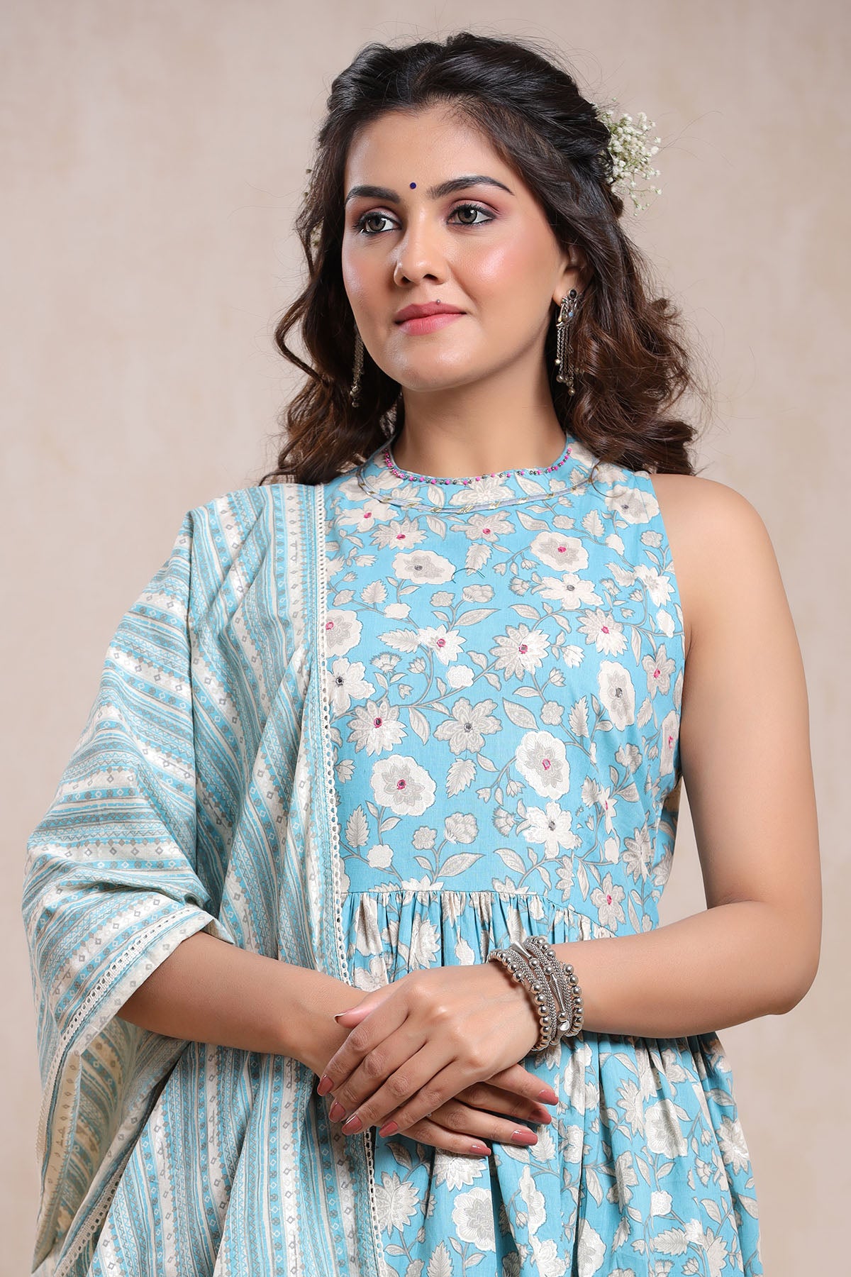 Woman wearing a light blue floral dress with a matching dupatta on a beige background