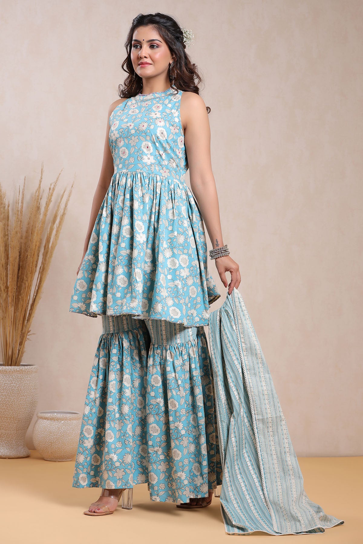 Woman wearing a blue floral dress with a matching dupatta against a beige background
