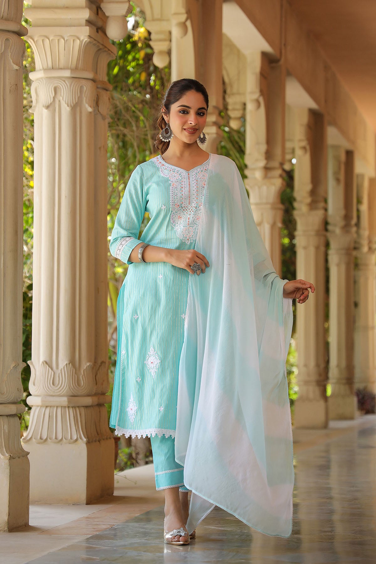 Woman in a light blue traditional outfit with a white dupatta standing in an architectural setting.
