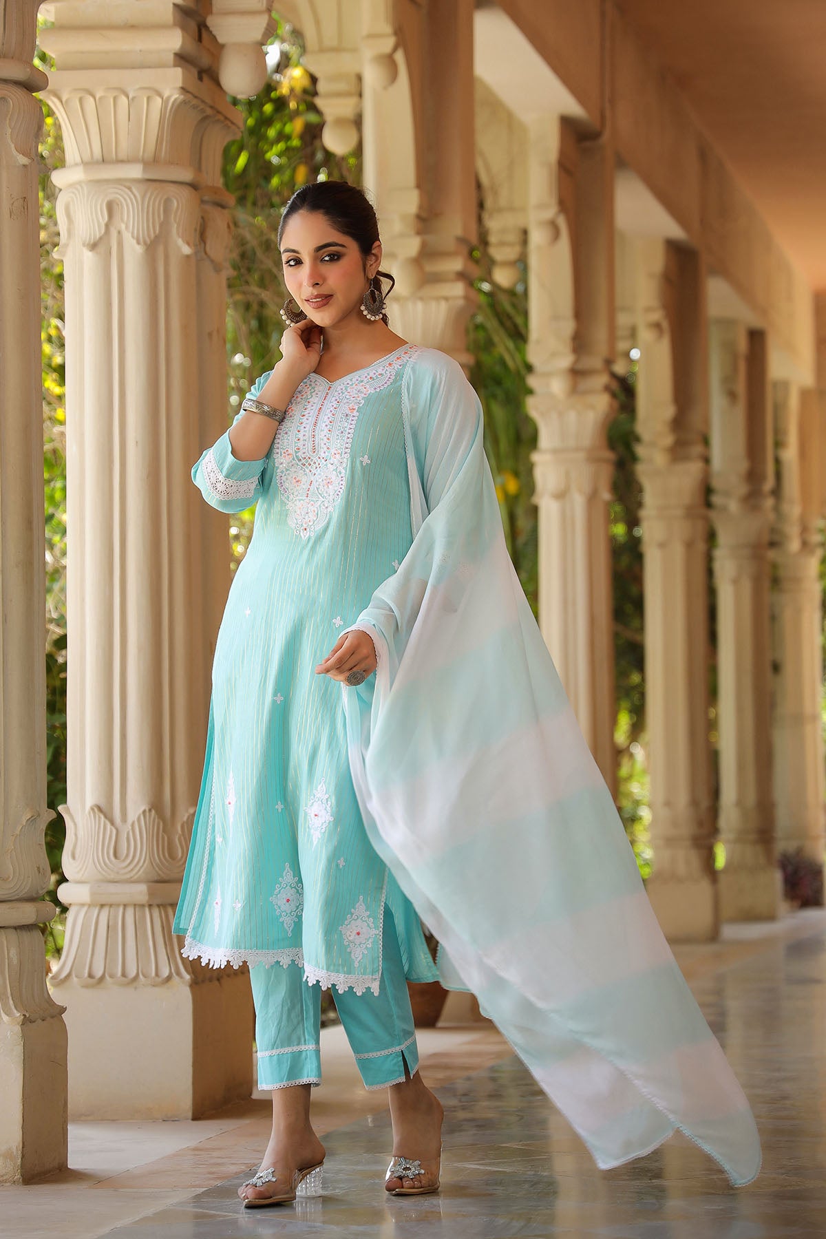 Woman in a light blue traditional outfit with white dupatta standing in an architectural setting.