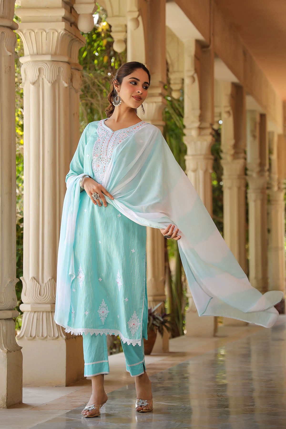 Woman in a light blue traditional outfit with a white dupatta standing in an architectural setting.