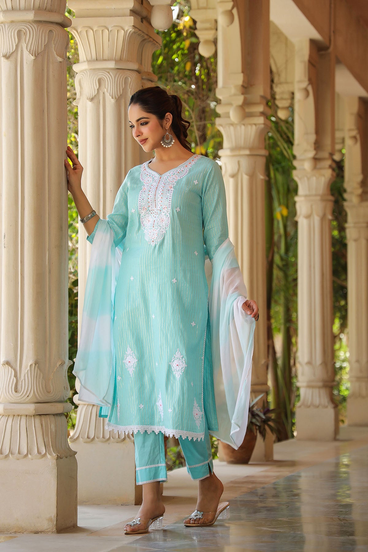 Woman in a light blue traditional outfit standing in an architectural setting with columns.