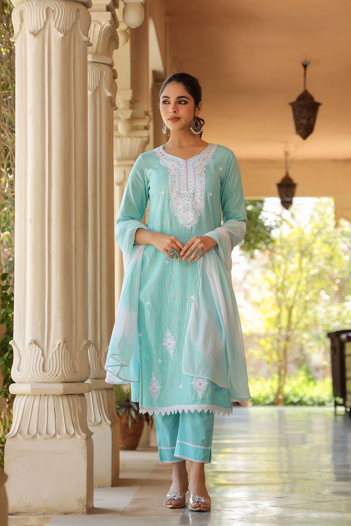 Woman in a light blue traditional outfit standing in a decorative outdoor setting.