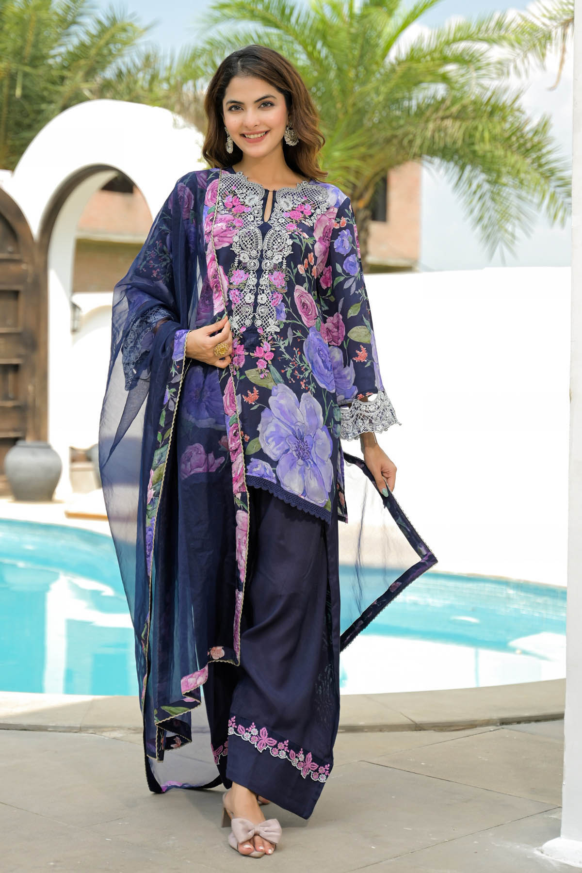Woman in a floral dress standing by a pool with palm trees in the background