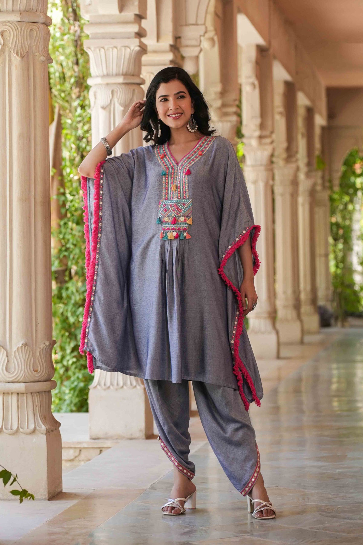 Woman wearing a traditional outfit with embroidered top and harem pants in an outdoor setting.