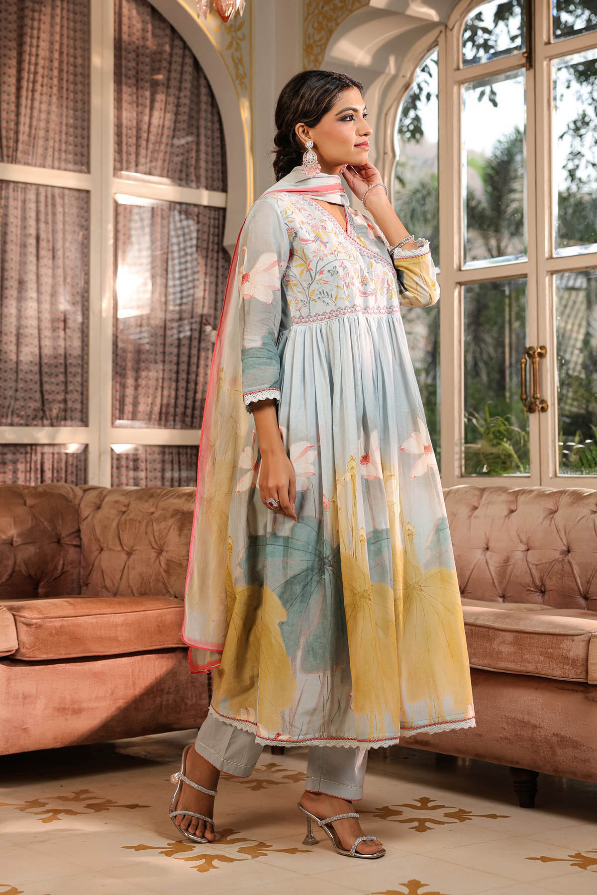 Woman in a traditional outfit standing in a room with large windows and a couch.