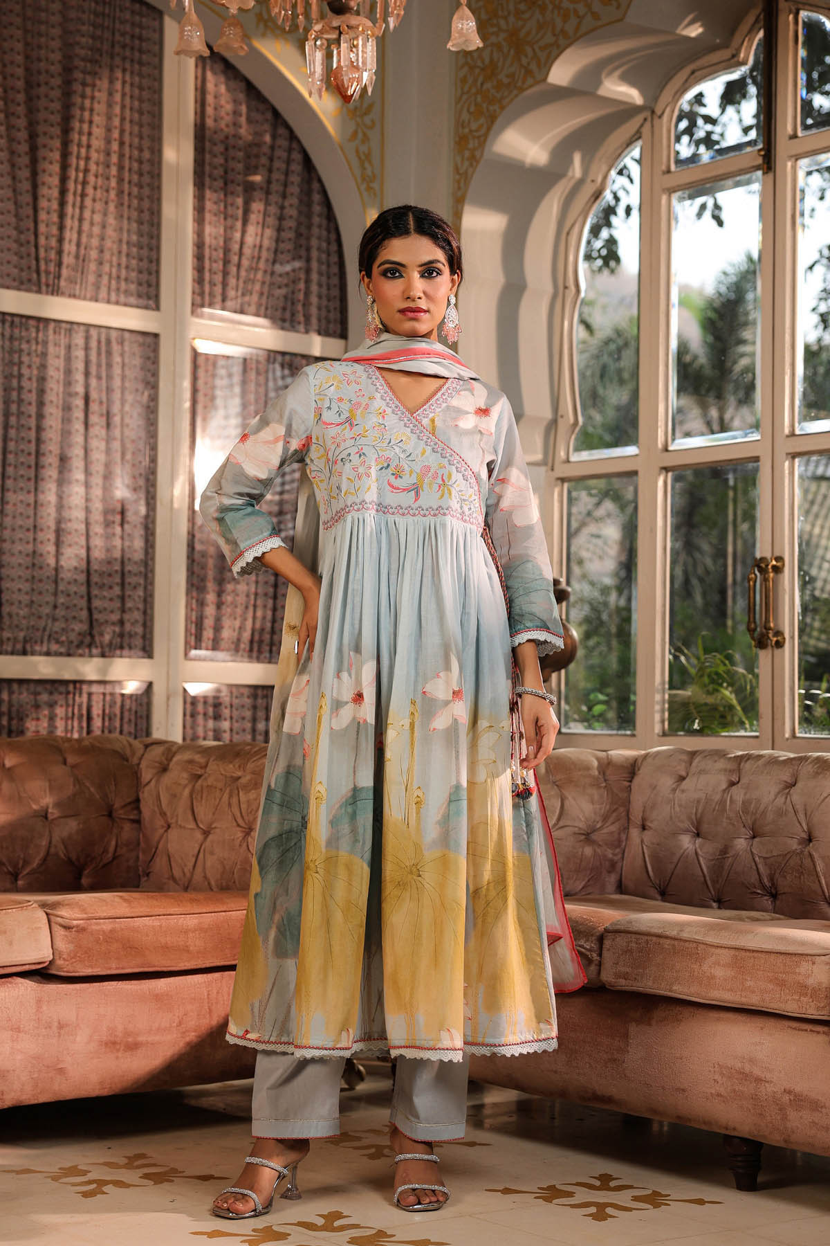 Woman in a traditional outfit standing in a decorated room with large windows.