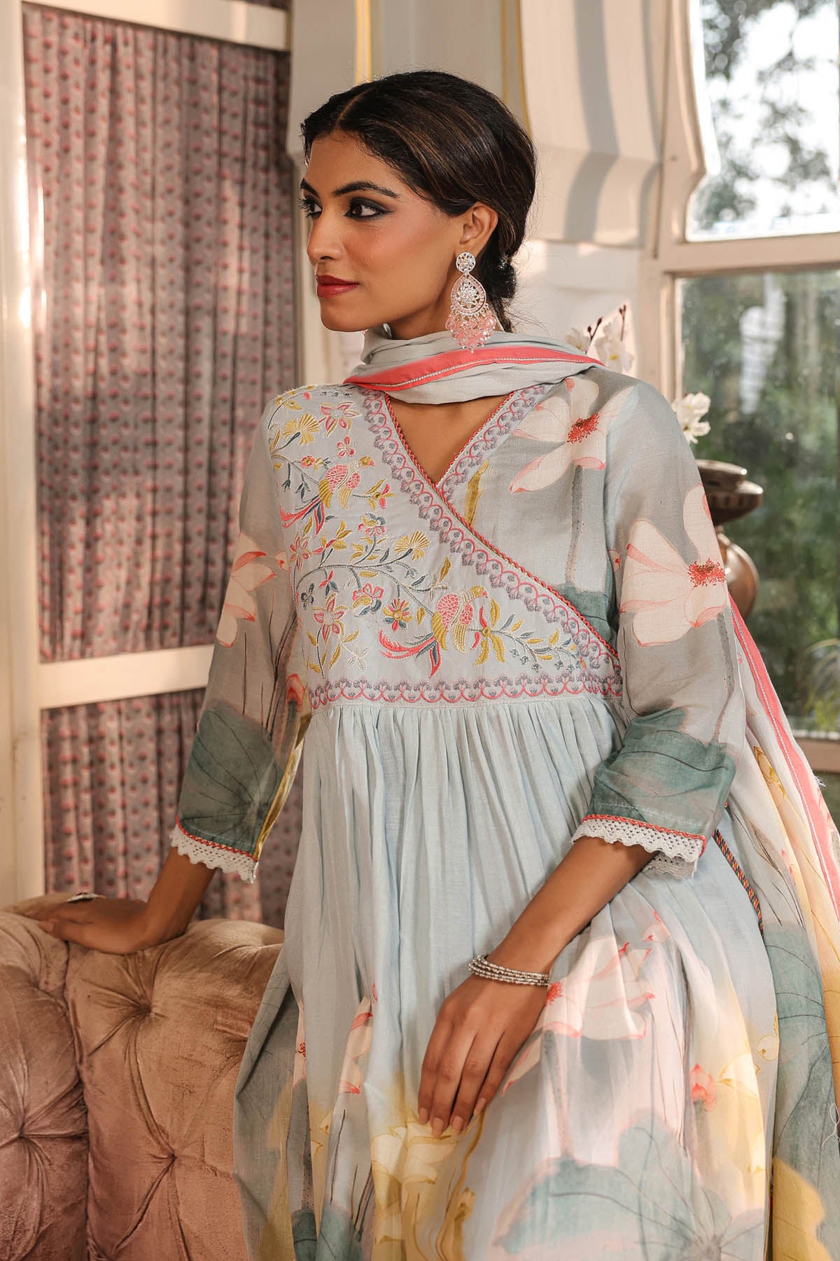 Woman wearing a light blue embroidered traditional outfit with a pink dupatta in an indoor setting.