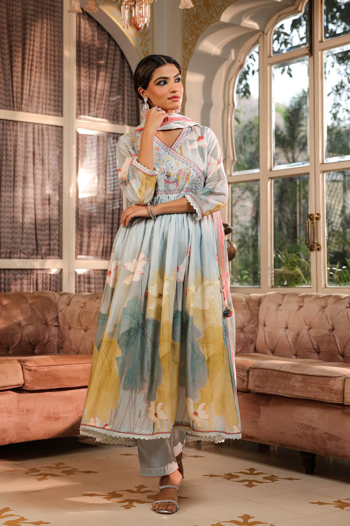 Woman in a floral dress standing in a stylishly decorated room with large windows.