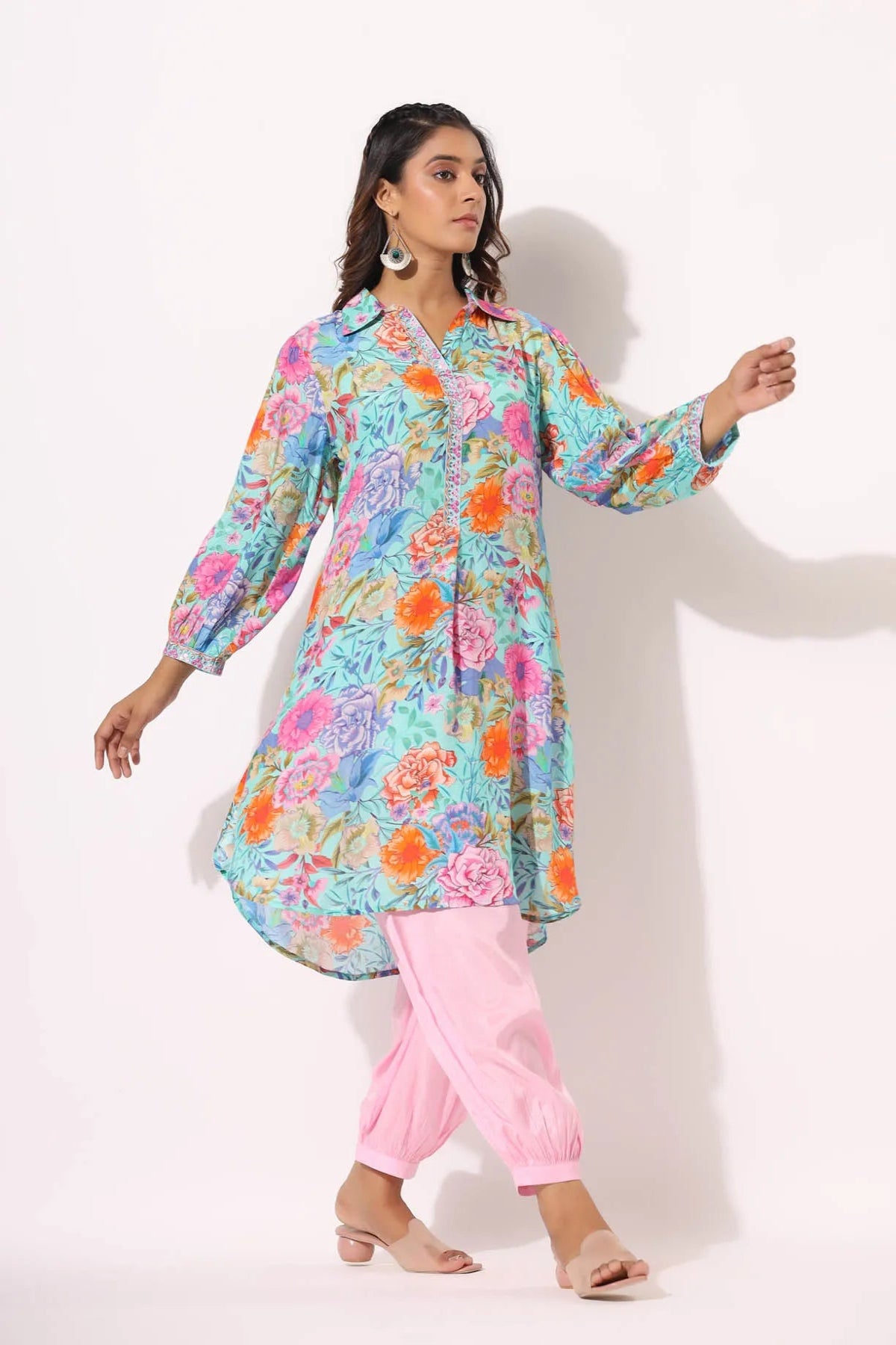 Woman wearing a colorful floral kurta with pink pants on a white background