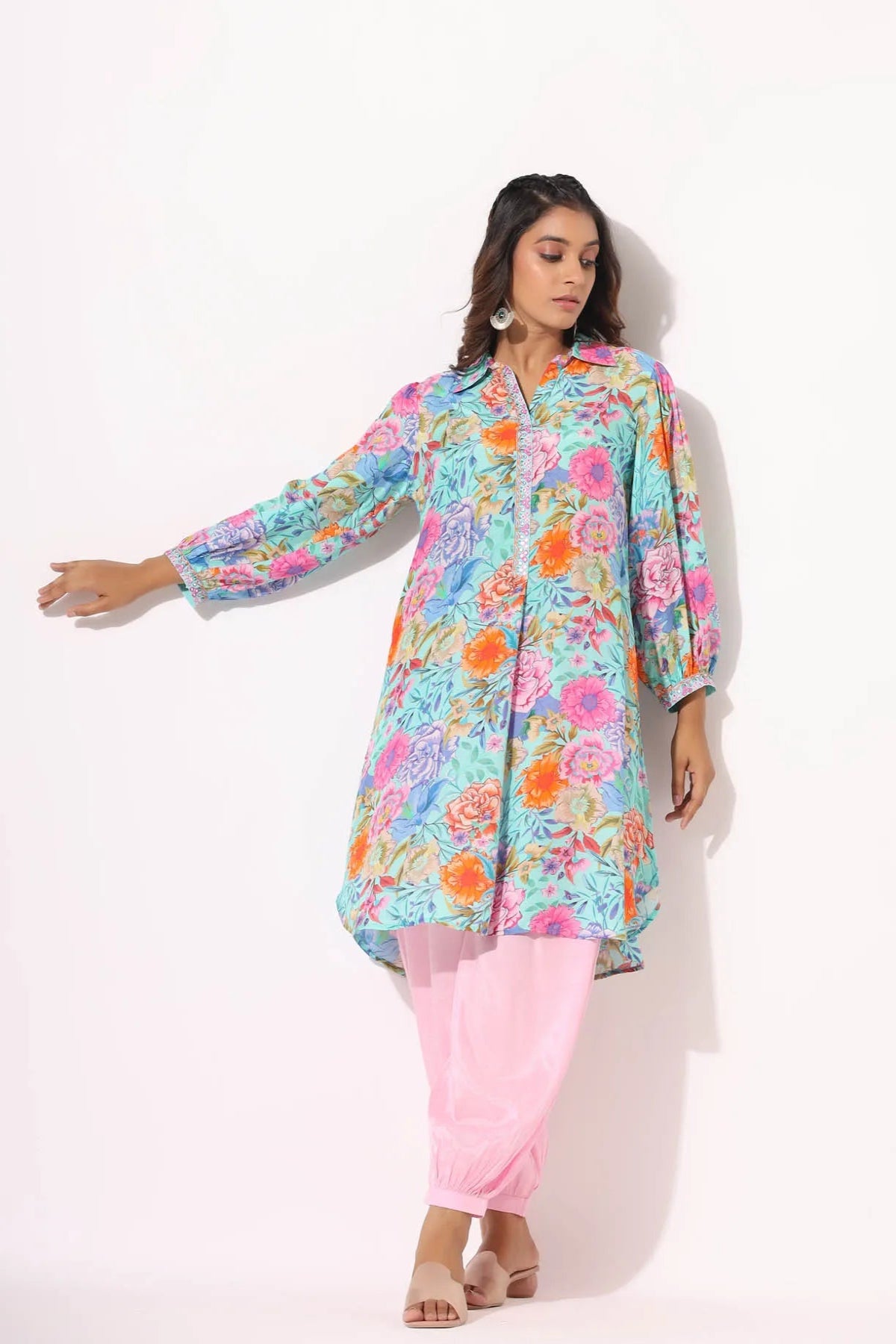 Woman wearing a colorful floral top and pink pants on a white background