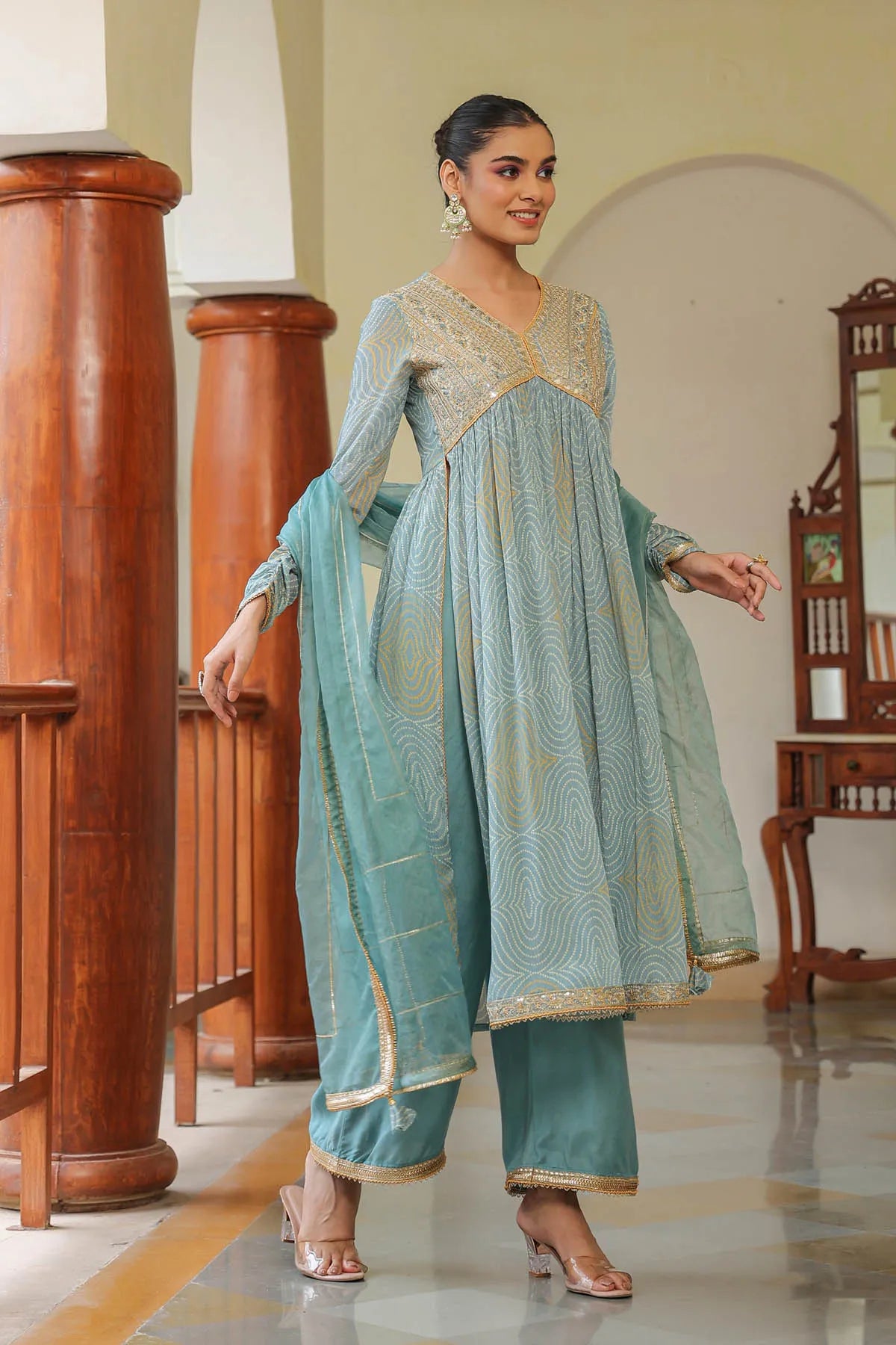 Woman in a light blue traditional outfit with gold patterns standing indoors.