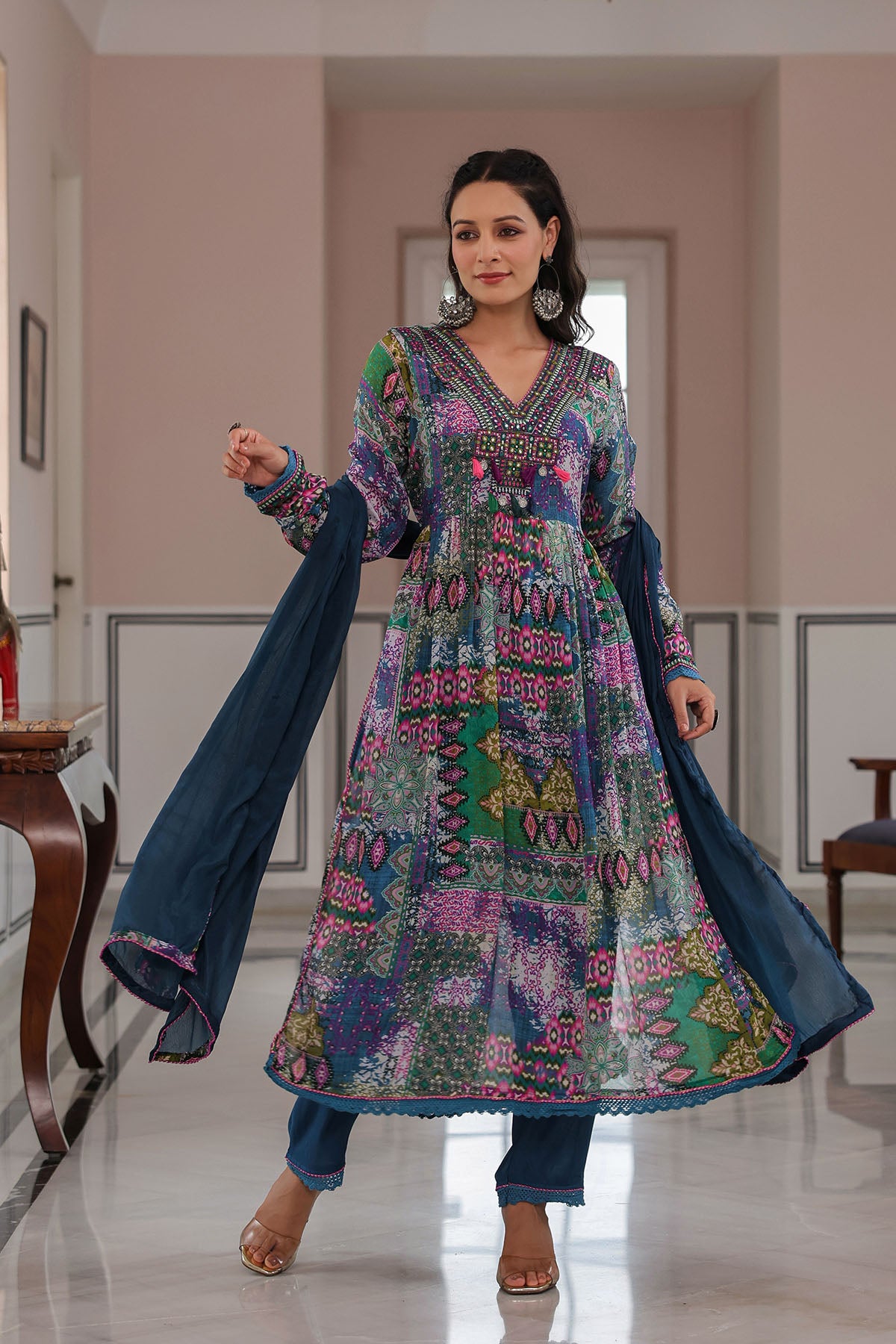 Woman wearing a colorful traditional outfit with a patterned dress and blue pants in an indoor setting.