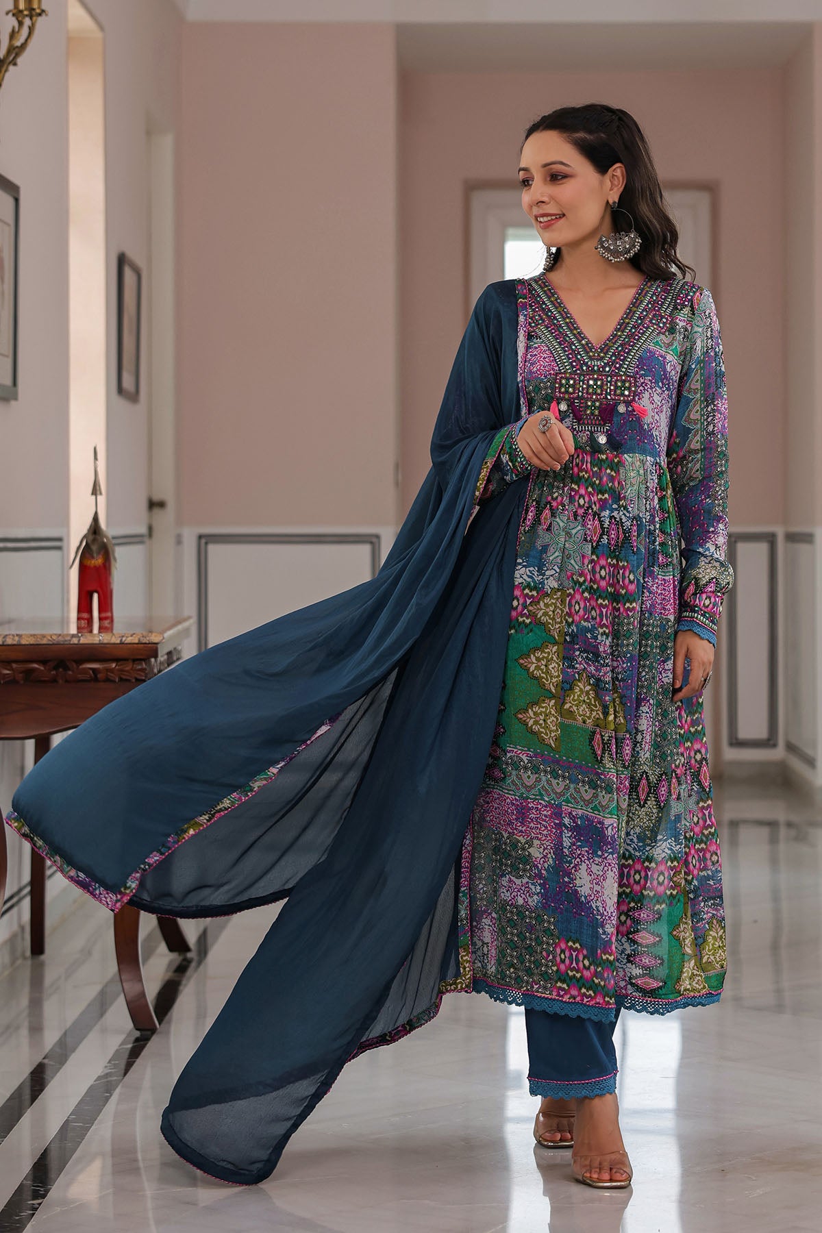 Woman wearing a colorful traditional outfit with a flowing blue dupatta in an indoor setting.