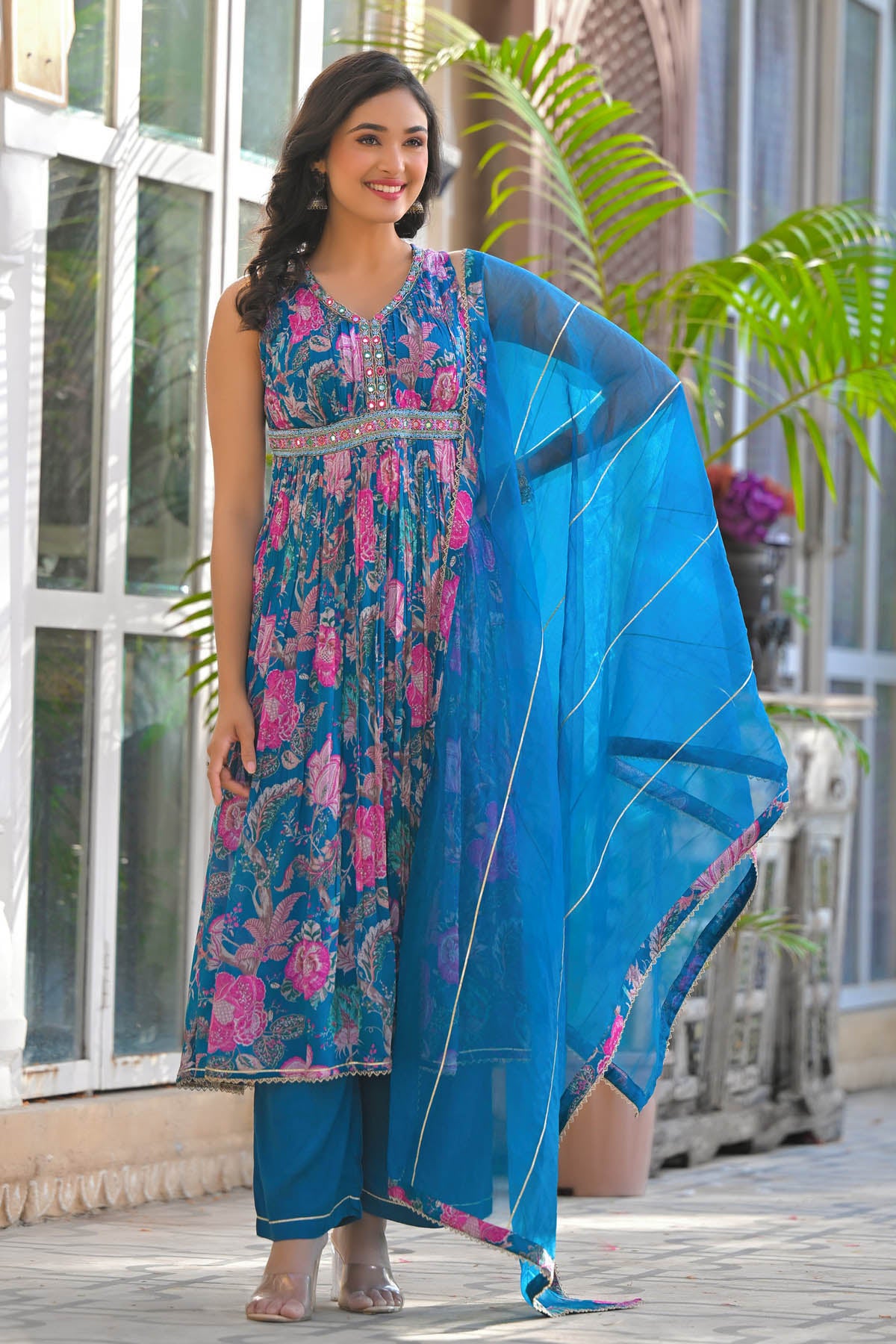 Woman in a blue and pink traditional outfit with a floral design, standing outdoors.