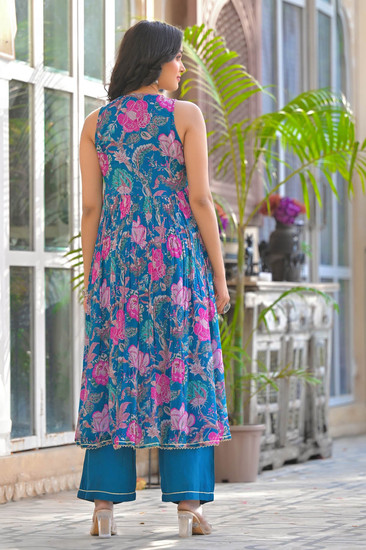 Woman wearing a blue floral dress standing in front of a glass door with plants.