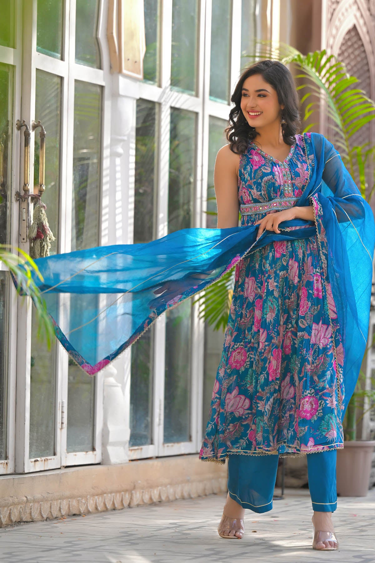 Woman in a floral dress with a blue dupatta standing indoors.