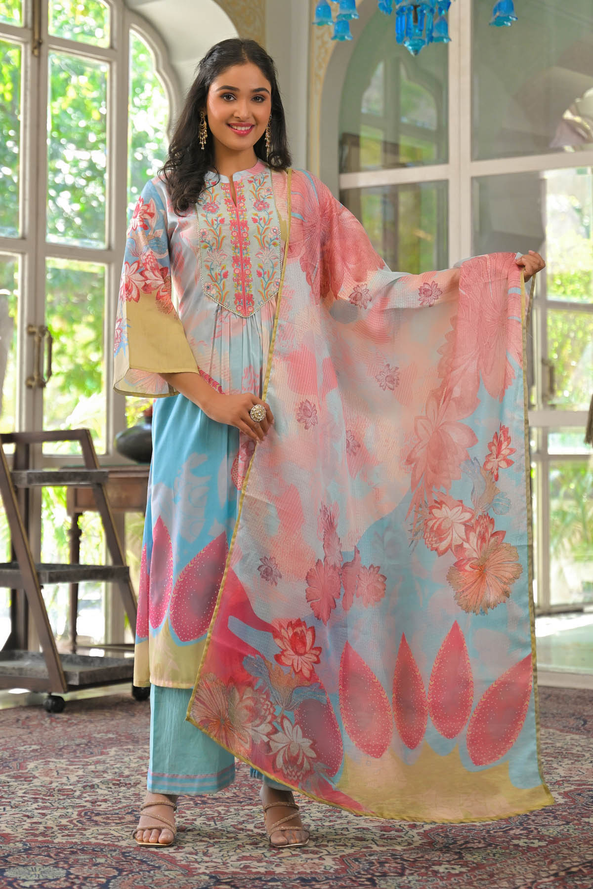 Woman holding a floral dress in a room with large windows.