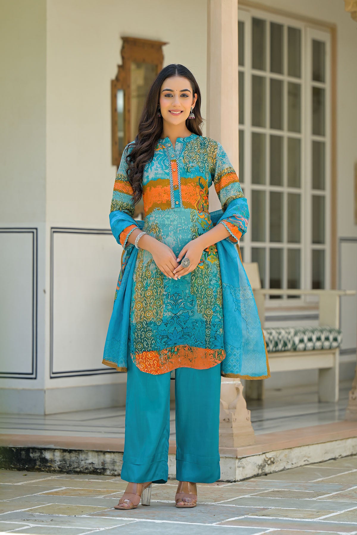 Woman wearing a blue and orange traditional outfit standing in a decorative indoor setting.