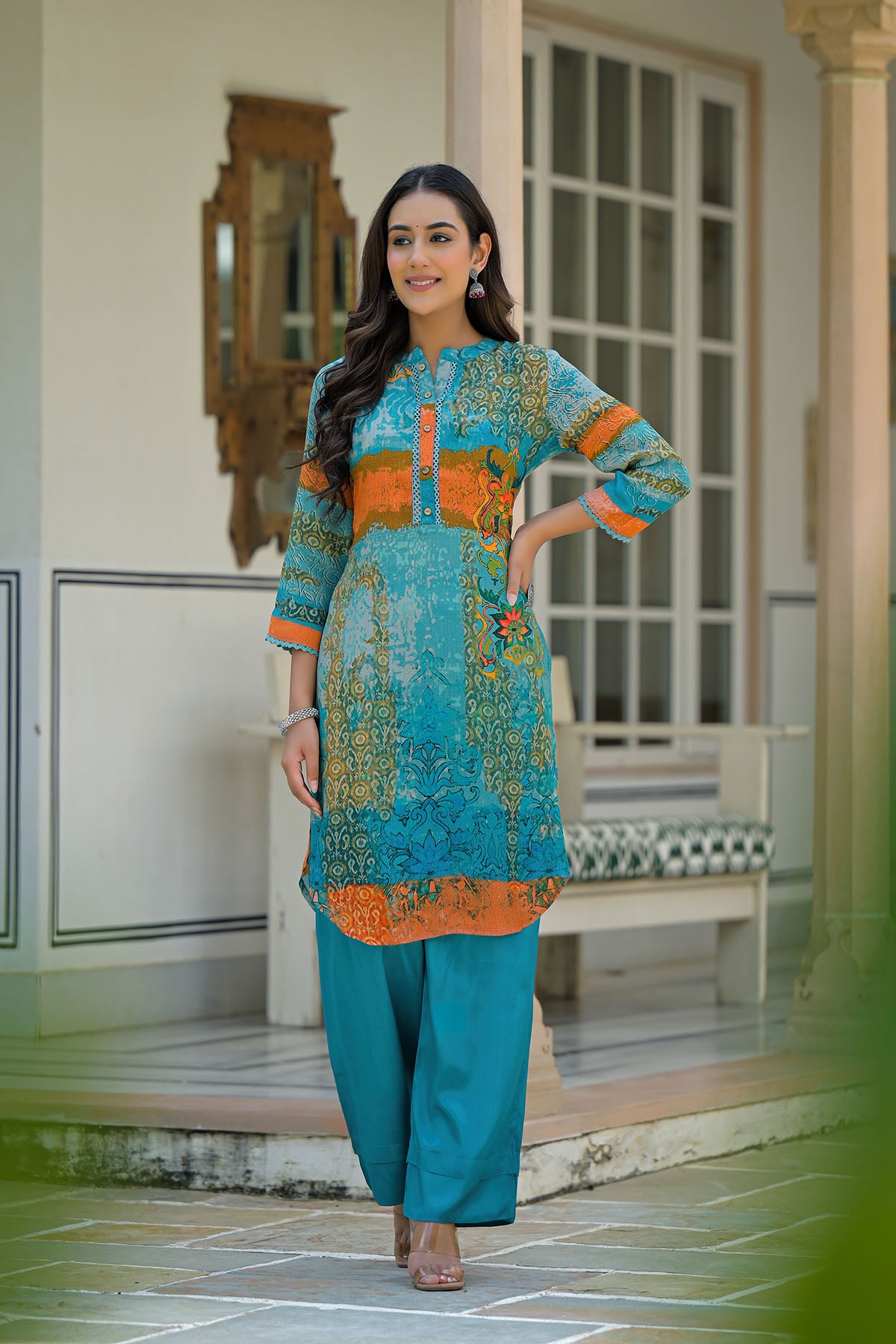 Woman in a colorful traditional outfit standing in a decorative indoor setting.