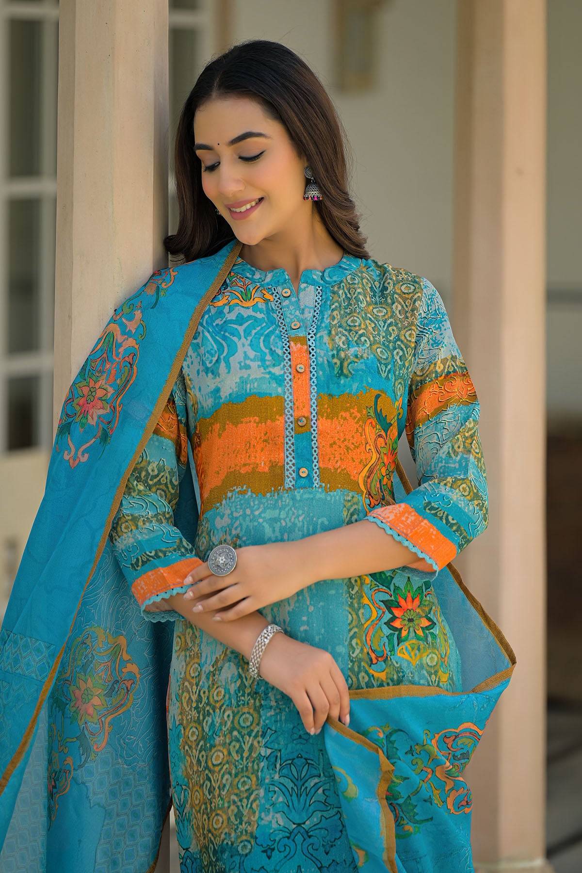 Woman wearing a blue and orange embroidered traditional outfit with a matching shawl.