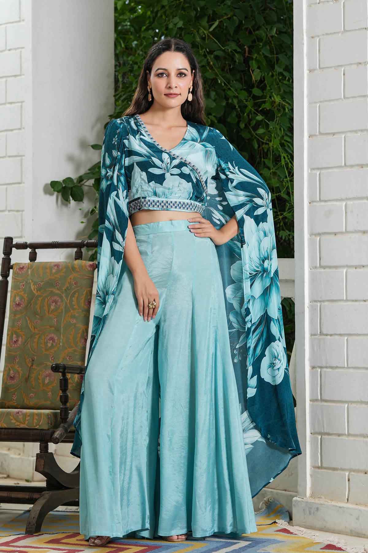 Woman in a teal traditional outfit with a floral shawl standing in a doorway.