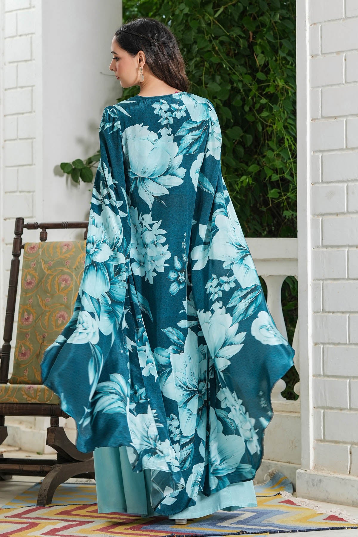 Woman wearing a blue floral dress standing in a room with white walls and a chair.