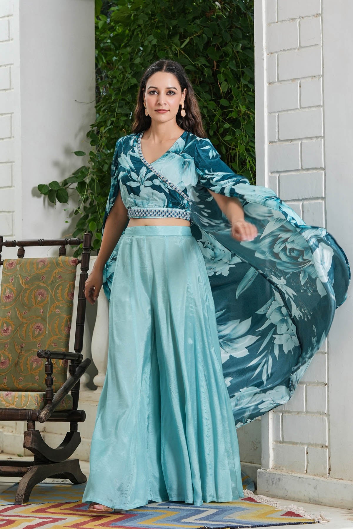 Woman in a teal floral outfit standing in a decorative outdoor setting.