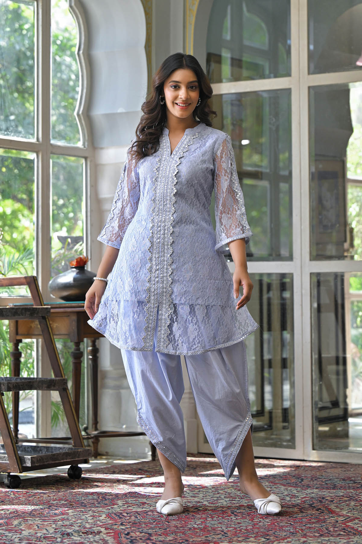 Woman wearing a light blue traditional outfit in a room with large windows.