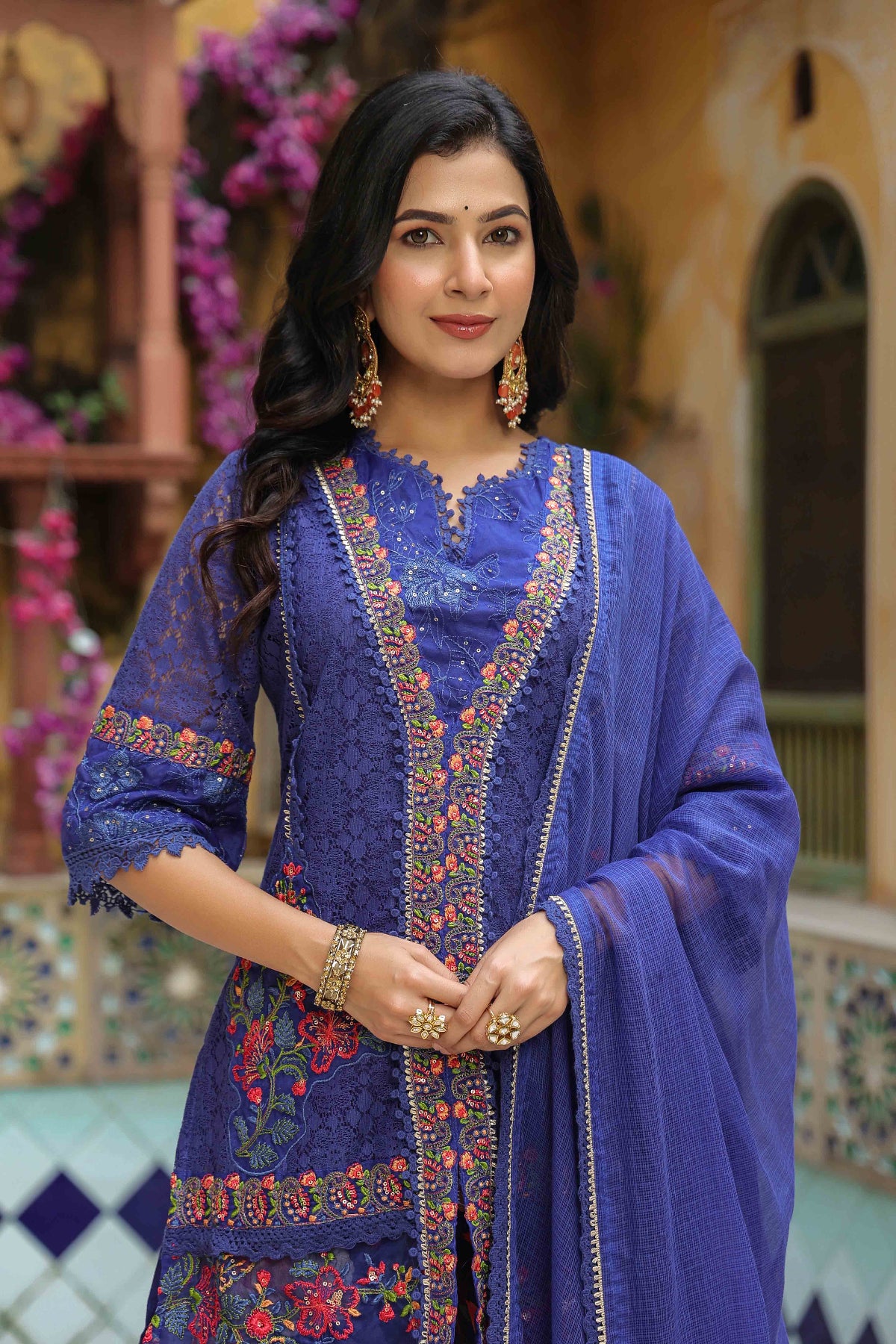 Woman wearing a traditional blue embroidered outfit with a decorative background