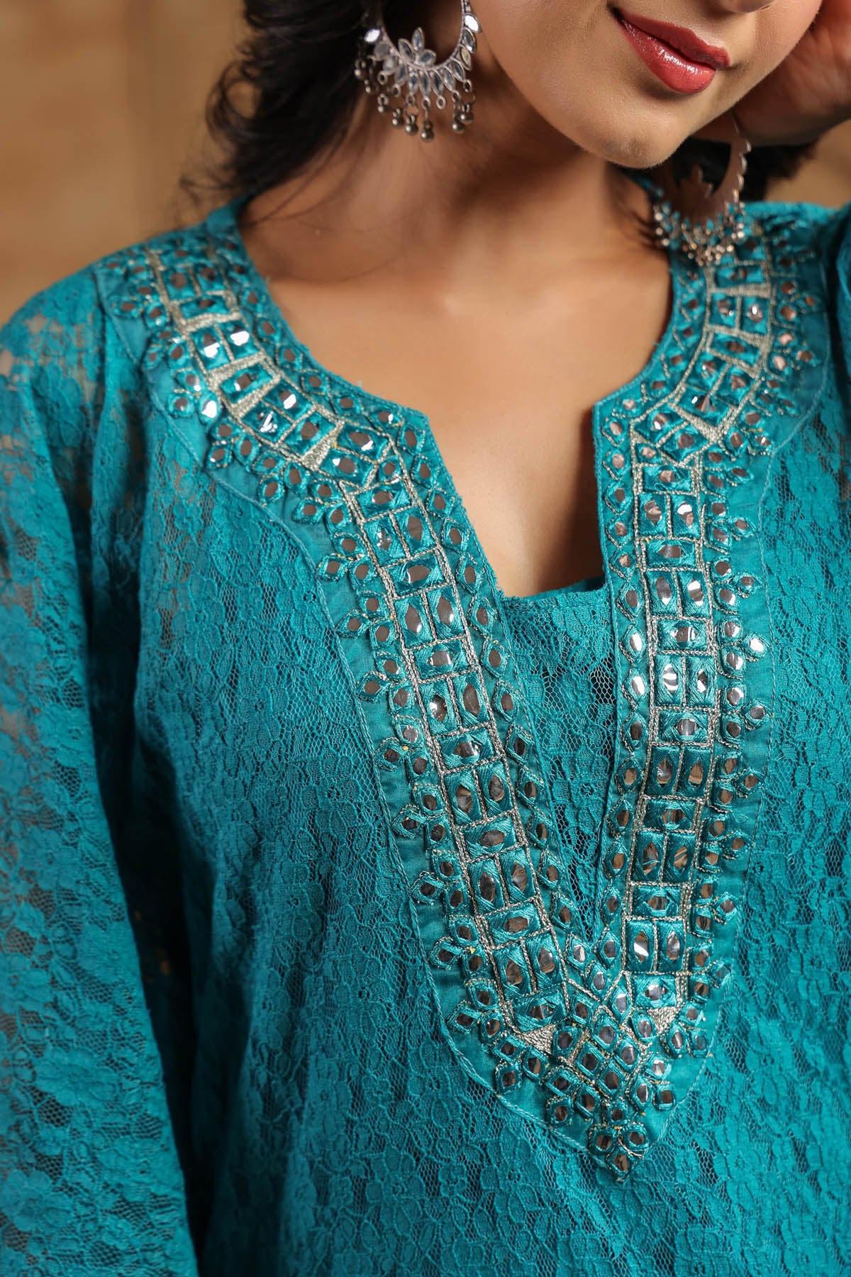 Close-up of a teal lace top with intricate beadwork on a blurred background