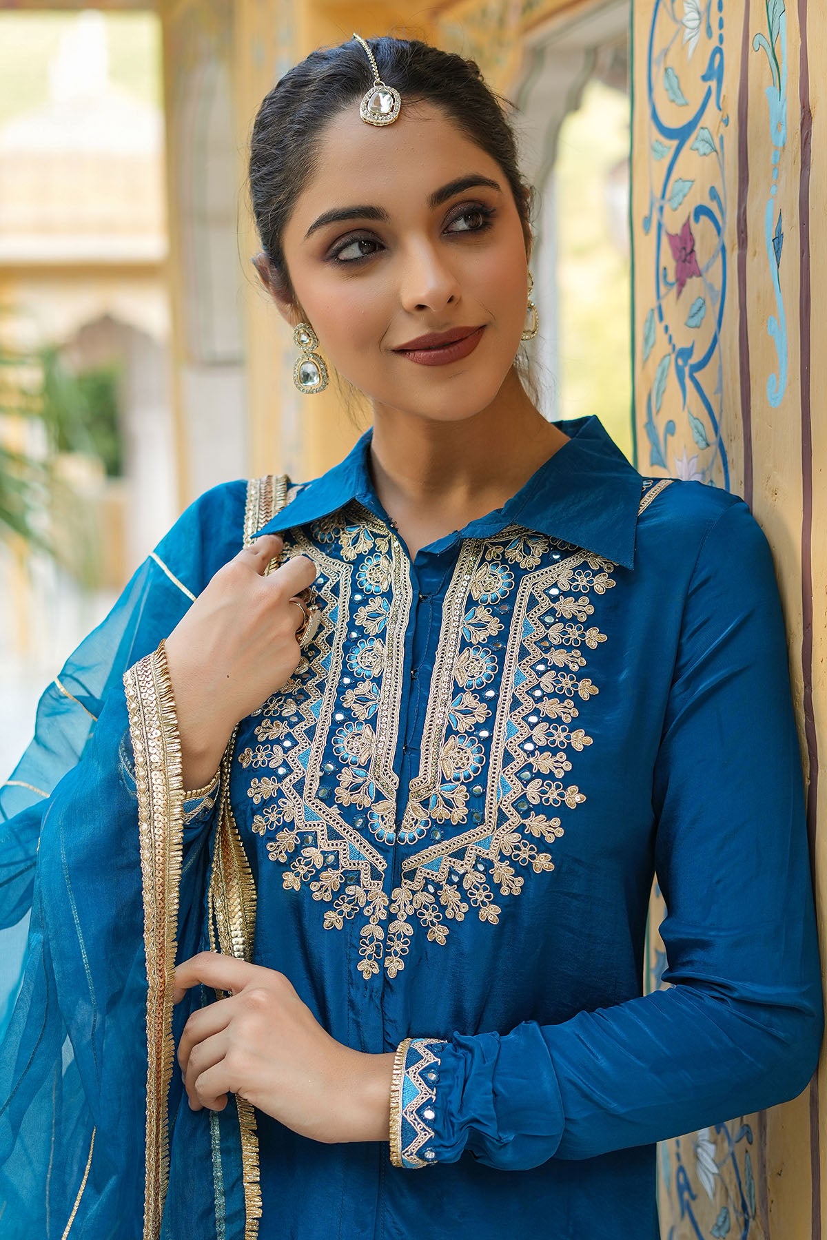 Woman wearing a blue embroidered traditional outfit with a decorative background