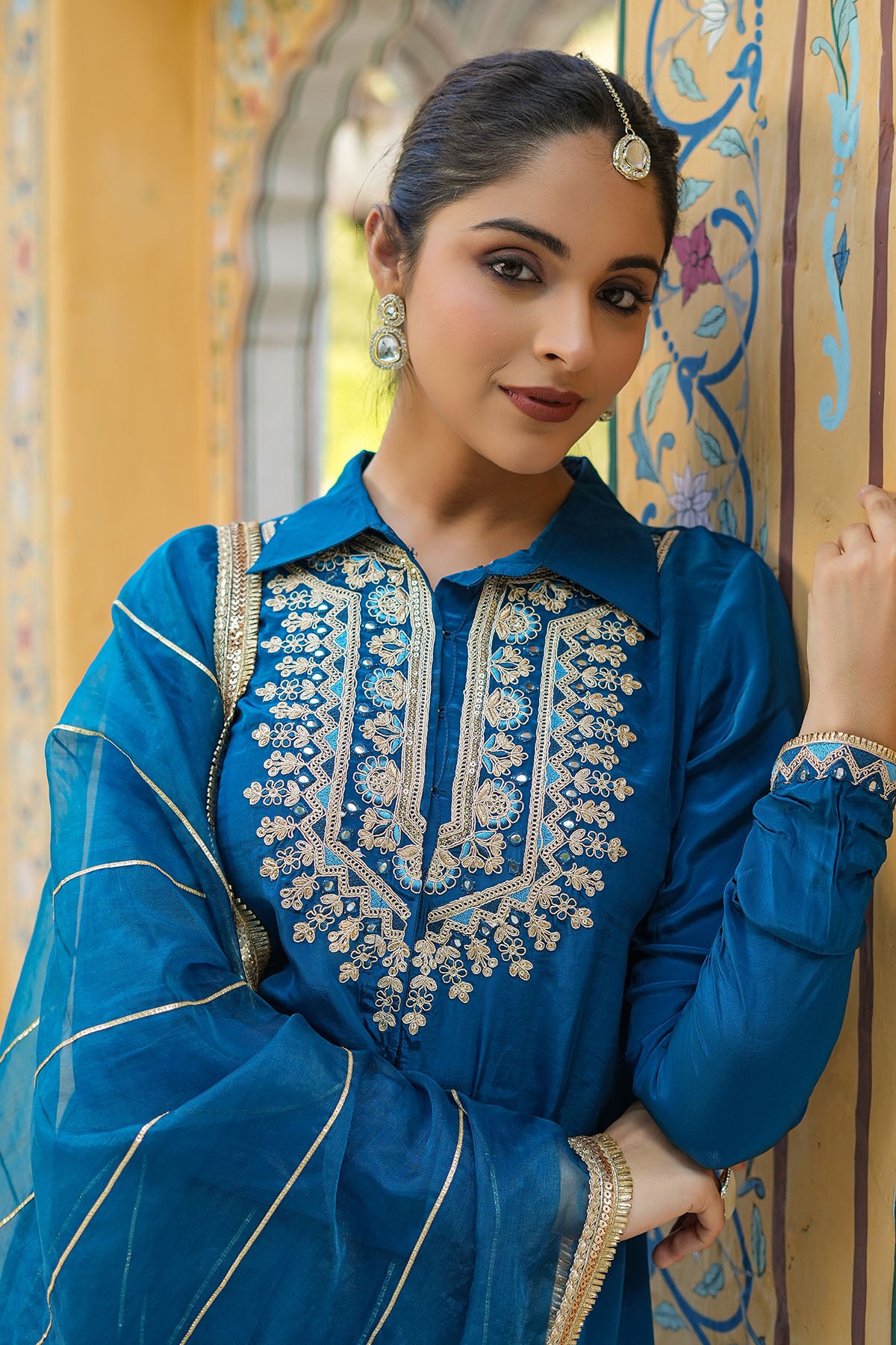 Woman wearing a blue embroidered traditional outfit in a decorative setting